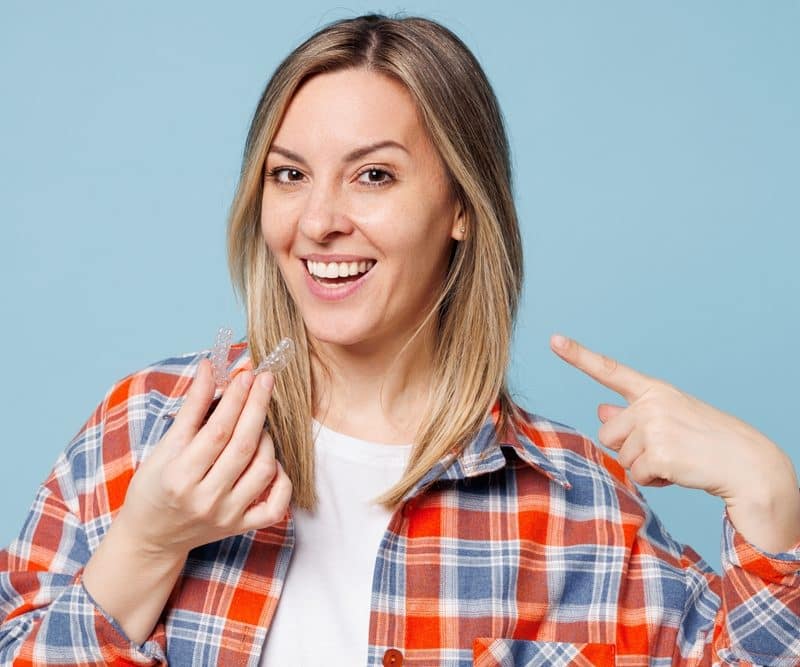 Woman smiling, holding invisible aligners, blue background