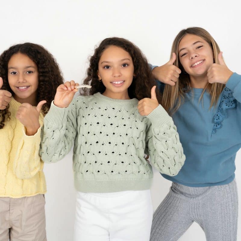 Three cheerful girls giving thumbs up, smiling at camera.