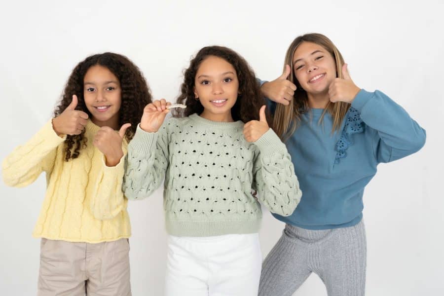 Three cheerful girls giving thumbs up, smiling at camera.